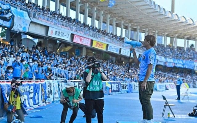 大久保嘉人氏がVチューバーのTシャツを着て等々力に降臨！ パイナップル3つを持って記念撮影に応じる！